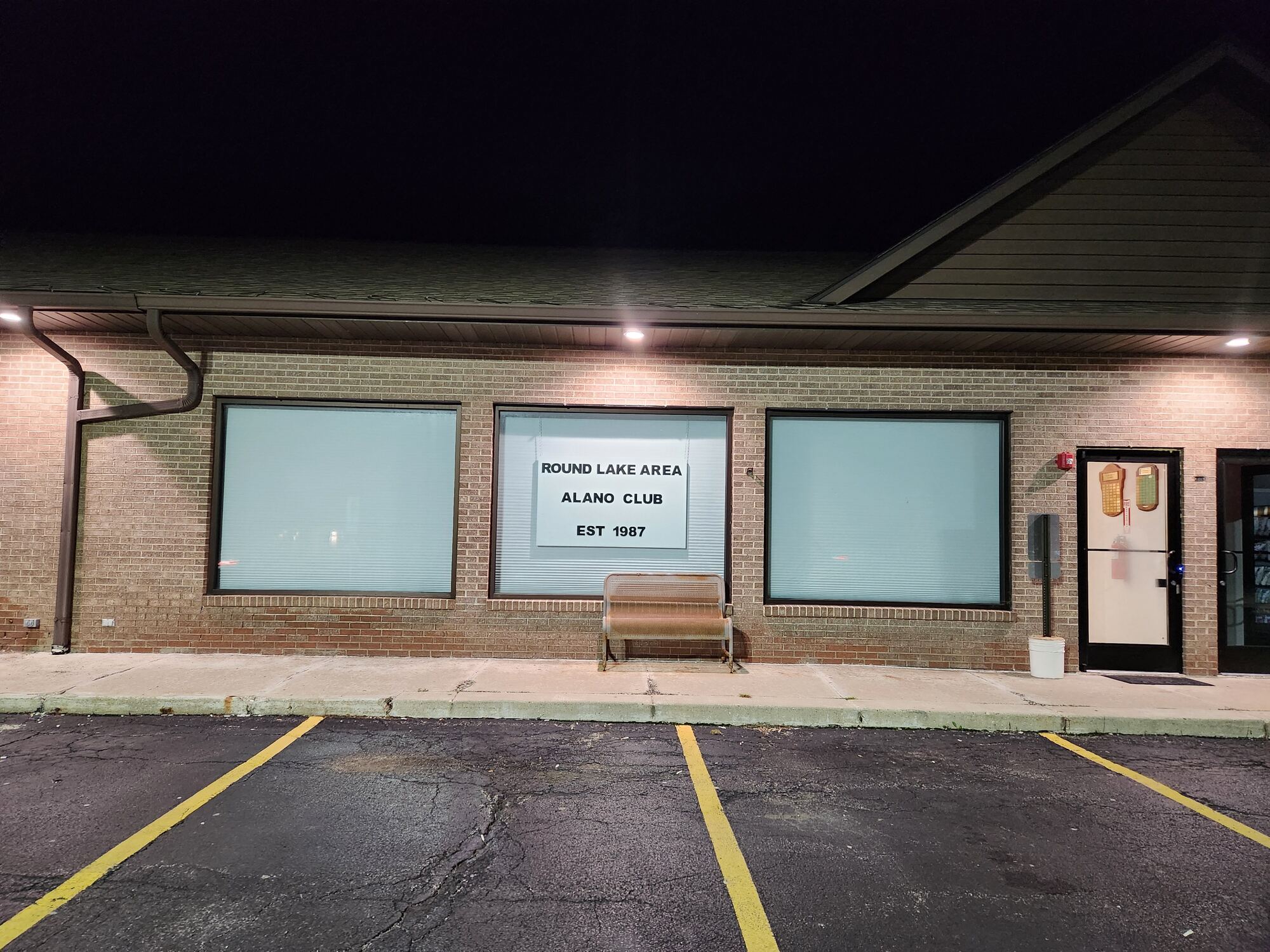 The Round Lake Area Alano Club storefront at night, its window sign reading Est. 1987